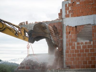 Backhoe demolishing a brick house